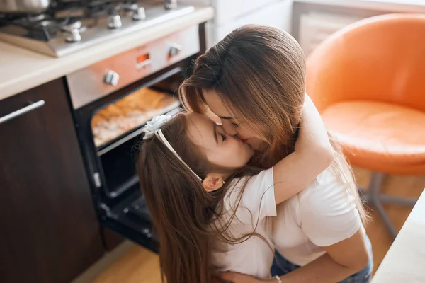 Αξιολάτρευτο ωραίο κορίτσι και ξανθιά μητέρα της φιλιά στο στόμα στην κουζίνα — Φωτογραφία Αρχείου