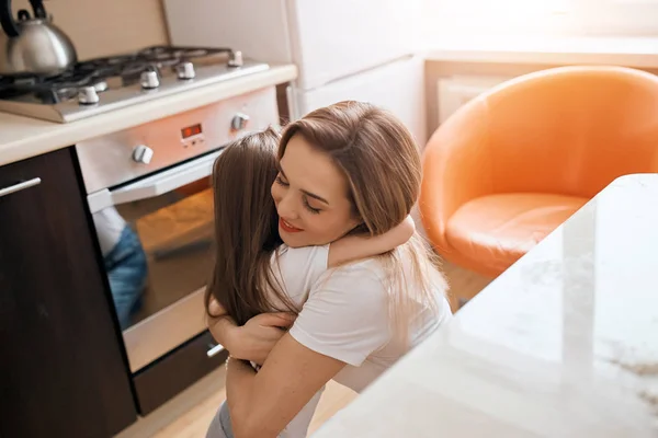 Linda criança e sua mãe abraçando, abraçando na cozinha — Fotografia de Stock