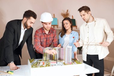 Miğferli genç mimar ortaklarına proje hakkında yeni fikirler veriyor.