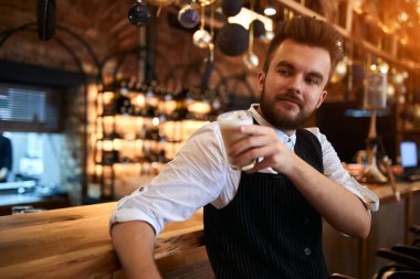 relaxed cheerful bearded waiter having a coffee break at workplace