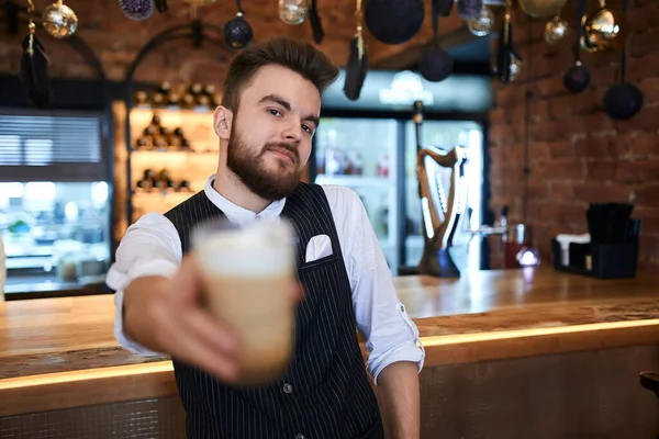 Joven barbudo barista guapo que ofrece una taza de sabroso cuppuchino — Foto de Stock