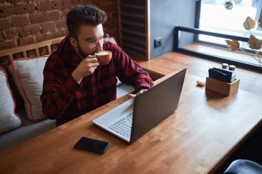 young handsome serious man with beard and moustache drinking coffee