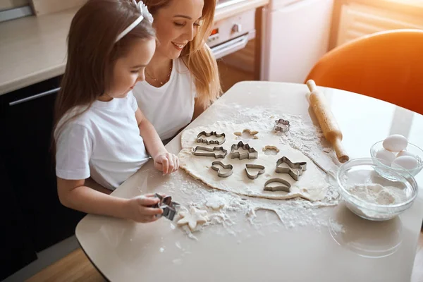 cheerful mother is proud of her kid who has cut different shapes for biscuits