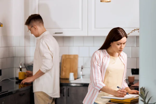 Chica seria atractiva leyendo y escribiendo en casa en la cocina —  Fotos de Stock