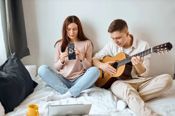 young man is fond of playing muscila instrumenst while woman fixing retro camera