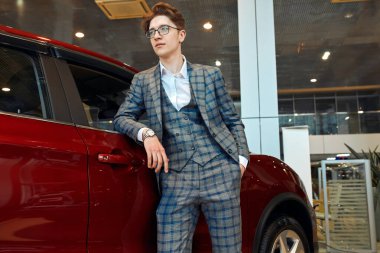 Başarılı genç adam modern lüks arabaya yaslanıyor ve yana bakıyor.