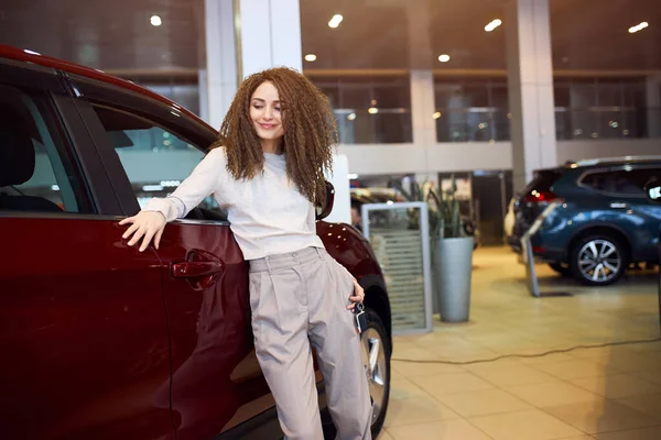 Mädchen mit welligem braunem Haar berührt ihr rotes Auto und lehnt sich darauf — Stockfoto