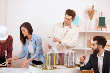 fair-haired man holding a blueprint and showing ot to bearded colleague