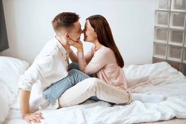 Alegre feliz homem e mulher em roupas acolhedoras beijando na cama . — Fotografia de Stock