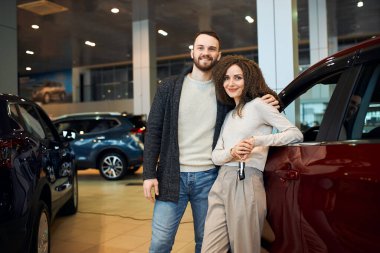 Anahtarları arabanın yanında gösteren mutlu ve çekici bir çiftin portresi.
