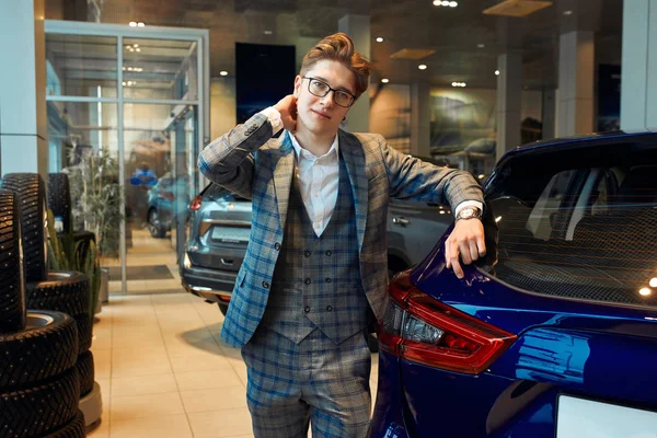 Man in glasses and fashion checked suit standing in light car dealership — Stockfoto