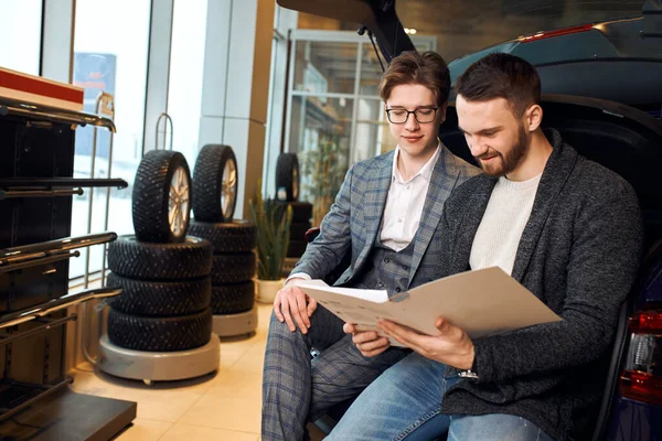 Junge, fröhliche Kundin sitzt mit Verkäuferin zusammen und analysiert die Unterlagen — Stockfoto