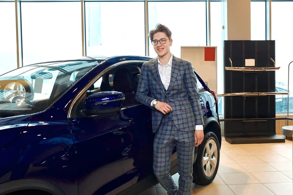 Man standing in front of a car in a showroom and posing to the camera — Stockfoto