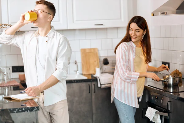 Handsome guy drinking coffee, his girlfriend preparing healthy breakfast — 스톡 사진