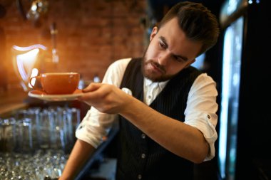 young serious waiter checking a cup of tea before serving it to clients