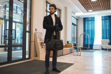 elegant man with a hand bag wearing a black stylish coat waiting for a client