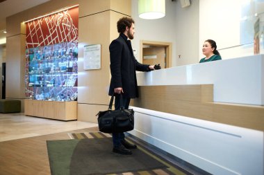 Young handsome businessman with abag in hands flirting with female receptionist