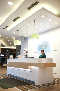 friendly female receptionist worker standing at hotel counter, greeting guests
