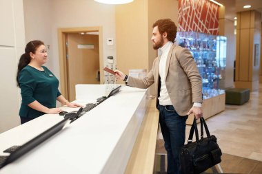 young attrcative bearded tourist holding a bag and giving passport to the female