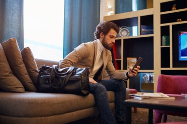 handsome bearded business man with suitcase sitting in hall of airport