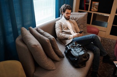 awesome man in jeans, beige jacket and roll-neck sending e-mail