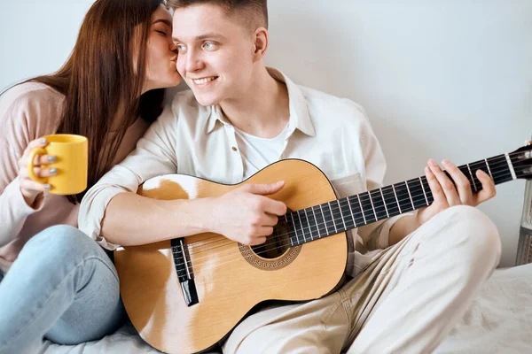 Menina beijando seu marido que está entretendo-a com instrumento musical — Fotografia de Stock