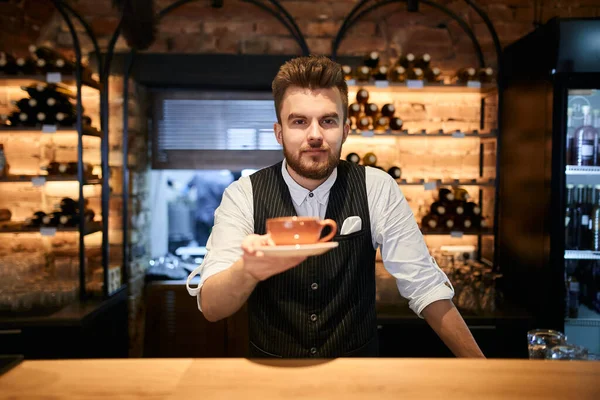 good looking waiter holding a cup on his palm and posing to teh camera