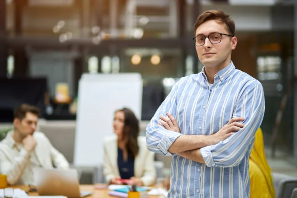 Cheerful young man with crossed arms in glasses looking at camera