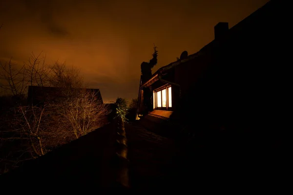 Mystische Fachwerkhausspitze mit beleuchteten Fenstern und Satteldach in der Nacht mit dunkelrot orangefarbenen Wolken Himmel, lange ausgesetzt — Stockfoto