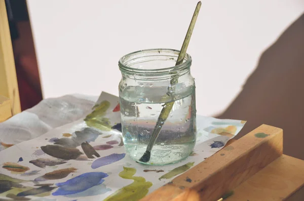 Konstnärliga utrustning: penslar, palett, tablett, burk med vatten och målningar på arbetsbordet i en artist studio. — Stockfoto