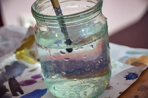 Pensel i rent vatten mellan ljusa färger i artist studio — Stockfoto