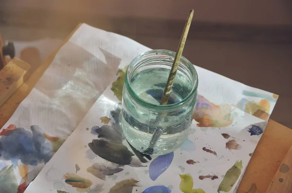 Pinceles artísticos en botella de agua sobre mesa con colores —  Fotos de Stock