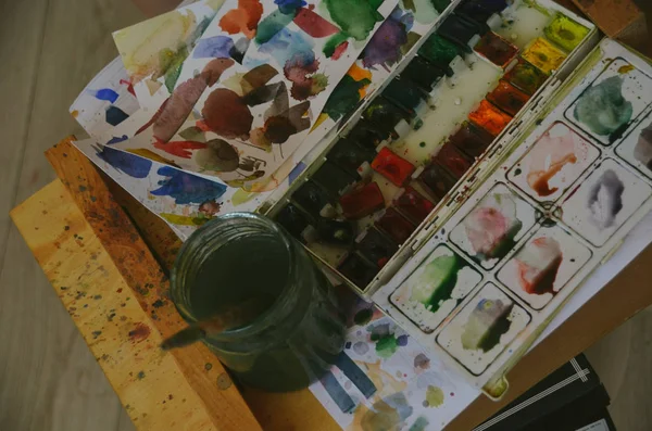 Set of watercolor paints and paintbrushes in glass with water in artist studio — Stock Photo, Image