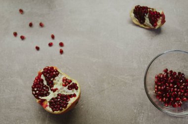 Gri arka planda taze olgun nar. Parlak kırmızı meyve tohumlarından oluşan minimalist düz tabaka