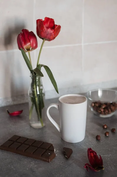 Biały Kubek Kawą Stole Jasnoczerwonymi Tulipanami Orzechami Mleczną Czekoladą Rano — Zdjęcie stockowe