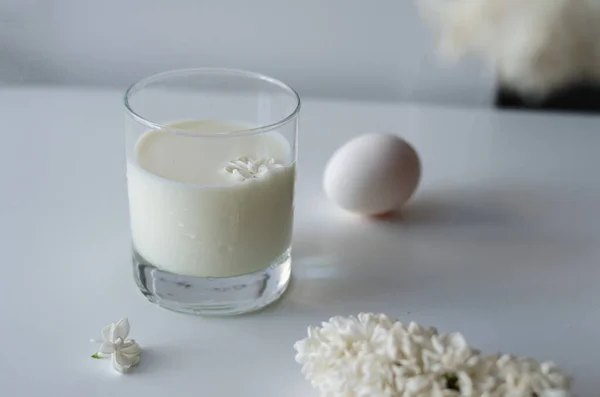 将淡紫色的白花放在白牛奶上 用玻璃杯和白蛋放在白桌子上 用美味的食物清洁平静的生活 早上的美餐 — 图库照片