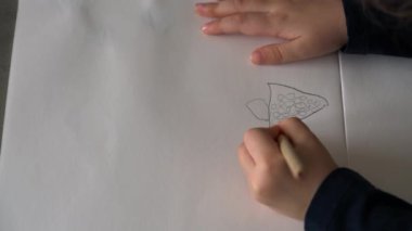 Küçük çocuk kalemle kağıda çiziyor.