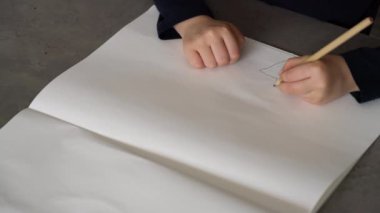 Küçük çocuk kalemle kağıda çiziyor.