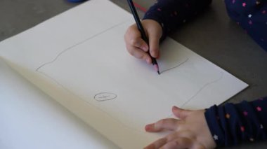 Küçük çocuk kalemle kağıda çiziyor.