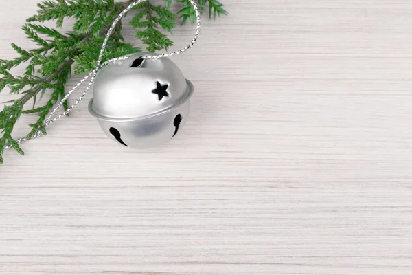 Green juniper branch with New Year's silver bell on a light wooden background. Minimalistic background for Christmas and New Year design — Stock Photo, Image