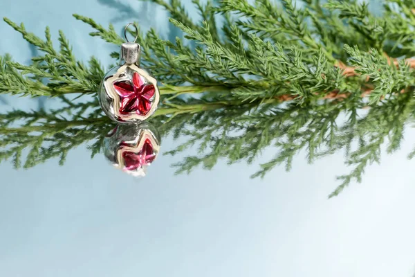 Aynalı yüzeyinde küçük eski bir Noel ağacı oyuncağı olan ardıç ağacının yeşil dalı. Noel ve Yeni Yıl tasarımı için şenlik arka planı. — Stok fotoğraf