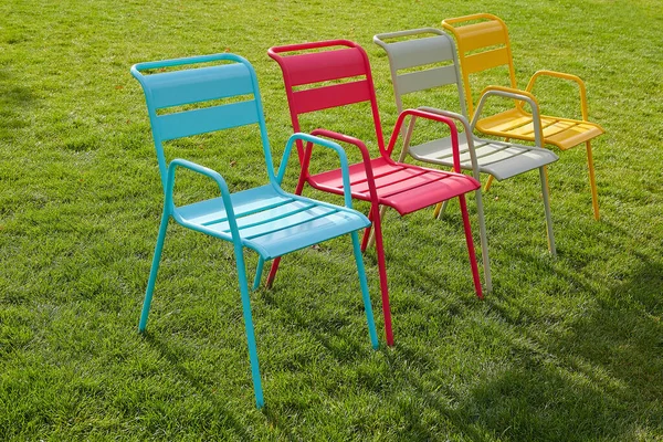 Four multi-colored chairs stand on a green lawn on a summer even — Stock Photo, Image