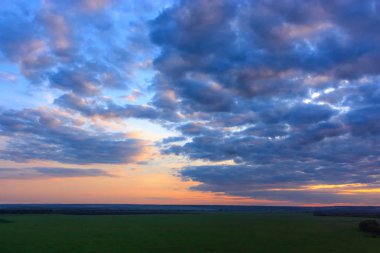 Harika bir gün batımı arka planı, harika altın ve pembe gökyüzü, akşam üstü inanılmaz mor bulutlar yeşil tarlalar üzerinde gün batımında.