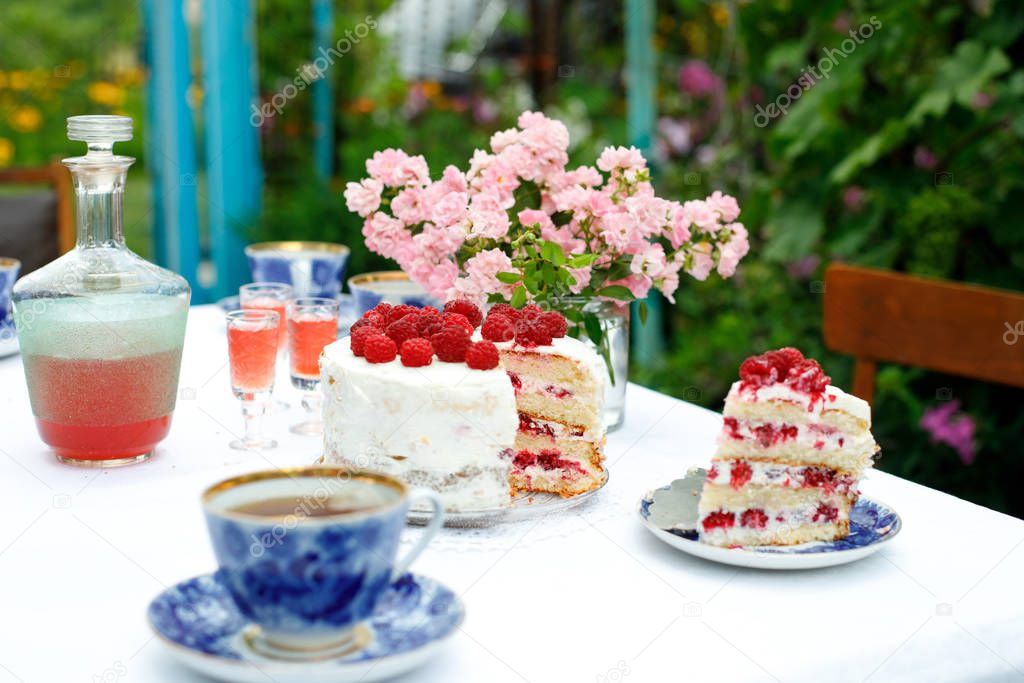 Laid holiday table in the summer garden. Cake, cups, glasses with liquor and a decanter on a table with a white tablecloth
