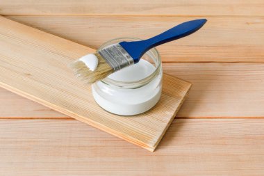 Beyaz boyalı mavi fırça cam bir kavanozun üzerinde, ışık panolarının arka planında, boyayla birlikte duruyor. Yakın çekim, seçici odaklanma