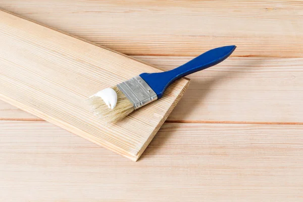 Der blaue Pinsel in weißer Farbe liegt auf einem hellen Holzbrett. Beginn der Reparaturarbeiten im Haus. Selektiver Fokus, Kopierraum — Stockfoto