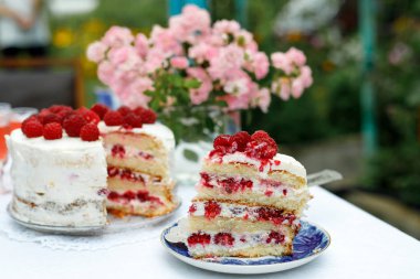 Bir dilim ev yapımı ahududulu kek, çay tabağının üzerinde, yaz bahçesindeki pastanın yanında. Seçici odak
