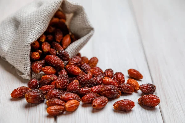 Bayas de rosa mosqueta secas al sol esparcidas de una bolsa de lino en una mesa de madera ligera. El concepto de medicina tradicional, tratamiento con plantas medicinales naturales. Primer plano. Copiar espacio —  Fotos de Stock