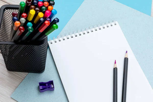 Colored pencils in a black office cup, purple pencil sharpener, a pair of sharpened pencils and a notebook on sheets of color cardboard. — Stock Photo, Image