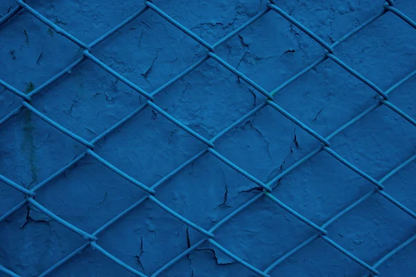 Metal wire grill on the background of an old blue wall with peeling paint. Mesh texture as a concept of confinement, unfreedom, or protection and security — Stock Photo, Image